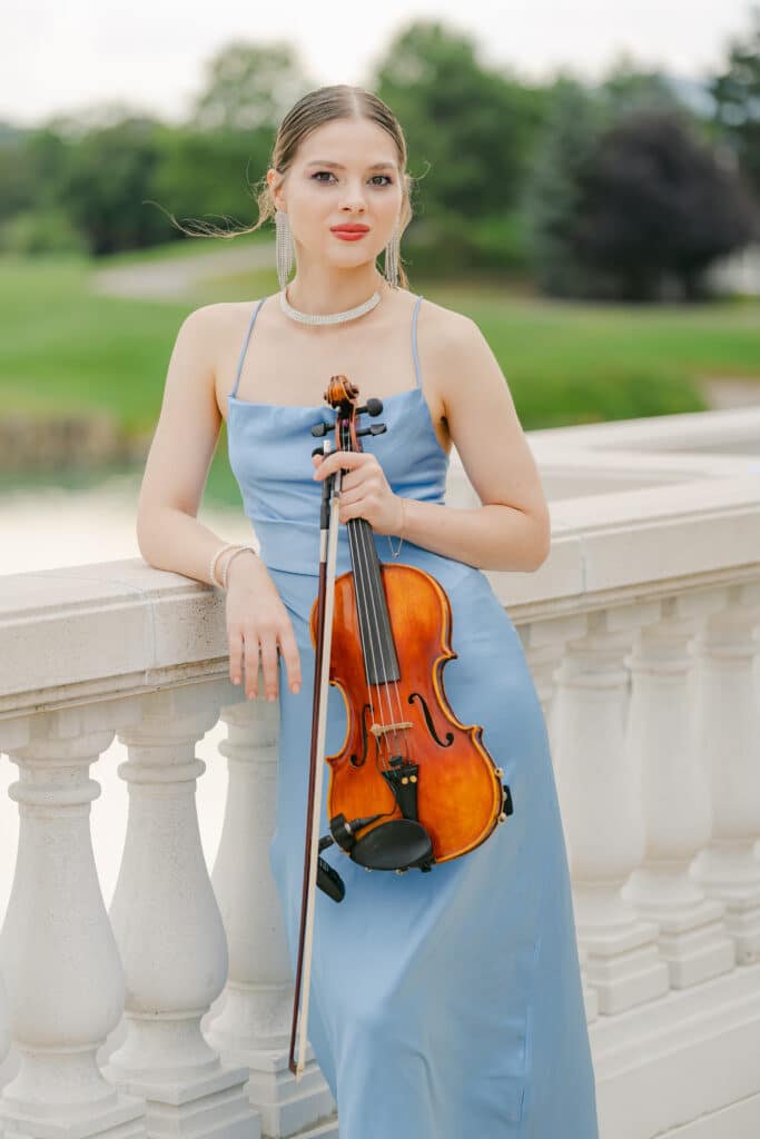 Violinistin in hellblauem Kleid mit Geige, stehend auf einer steinernen Balustrade