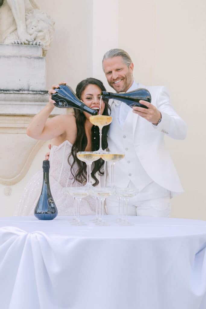 Anna Victoria Reiser und Paul Janke gießen Champagner in eine Pyramide aus Gläsern in der Villa Mosconi Bertani