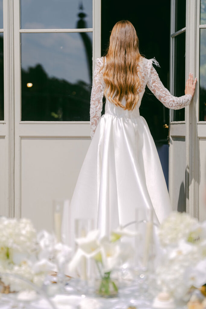 First Look Braut im Hochzeitskleid zwischen weißen Blumenarrangements

