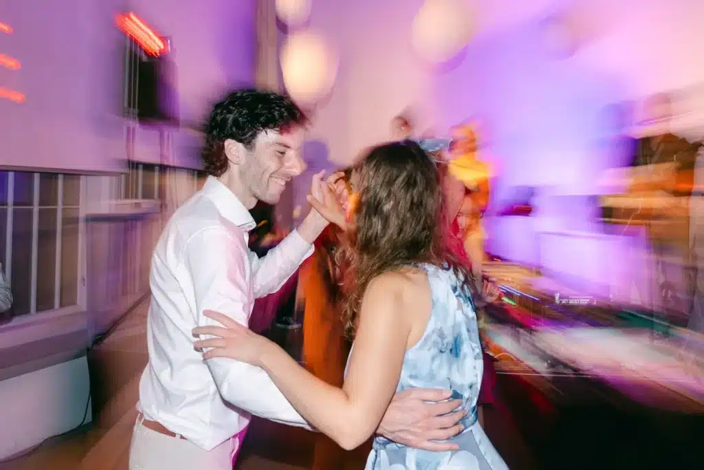 Bräutigam tanzt mit einem Gast im hellblauen Kleid im bunten Partylicht, Hochzeitsfeier in der Orangerie im Schlosspark Eisenstadt