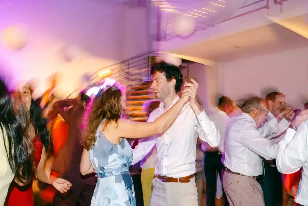 Bräutigam tanzt inmitten der Gäste auf der Tanzfläche im violetten Partylicht, Hochzeitsfeier in der Orangerie Eisenstadt