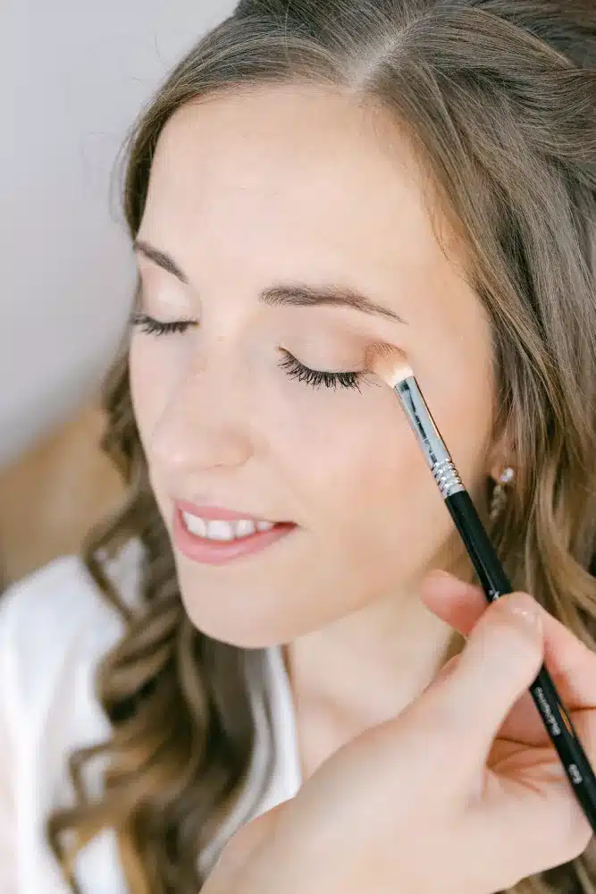 Braut mit geschlossenen Augen beim Auftragen des Lidschattens während des Getting Ready vor der Hochzeit in der Orangerie im Schlosspark Eisenstadt