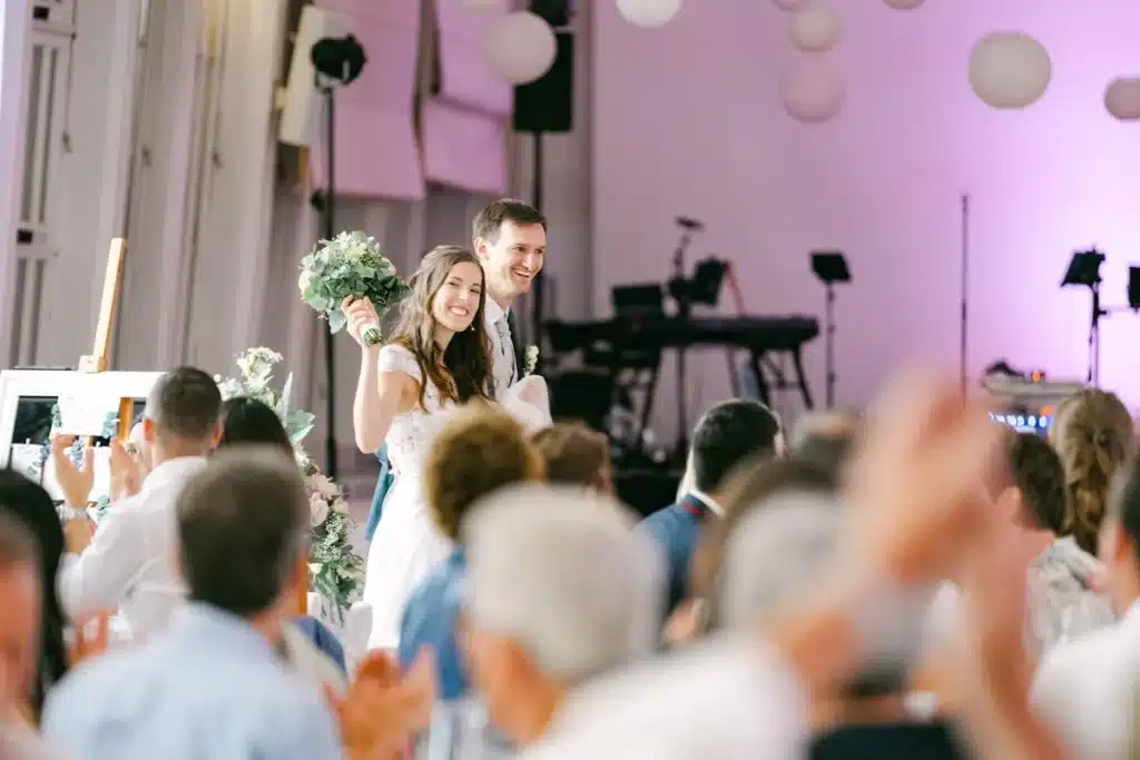 Brautpaar betritt den Festsaal der Orangerie Eisenstadt, die Gäste applaudieren, im Hintergrund die Bühne der Band