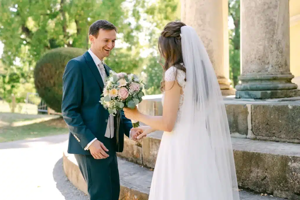 Brautpaar lacht sich beim First Look zwischen den Säulen des Tempels an, Hochzeit im Schlosspark Eisenstadt