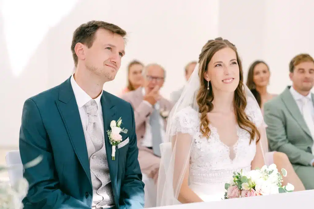 Brautpaar sitzt bei der Trauung vor den Gästen, der Brautstrauß liegt vor ihnen, Heiraten in der Orangerie im Schlosspark Eisenstadt