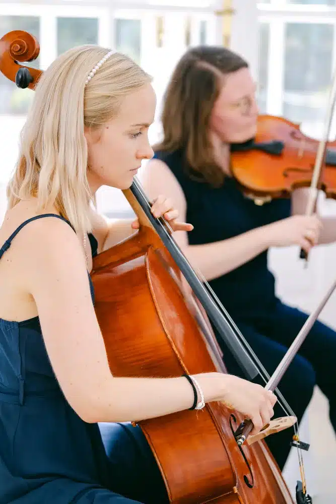 Cellistin und Geigerin in dunkelblauen Kleidern spielen während der Trauung in der Orangerie im Schlosspark Eisenstadt