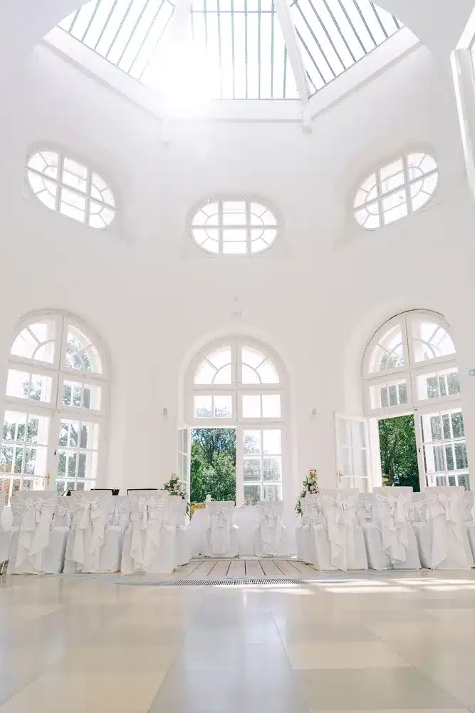 Trauraum der Orangerie Eisenstadt mit Rundbogenfenstern, Ochsenaugen und Oberlicht im Dach, Stuhlreihen in weißen Hussen