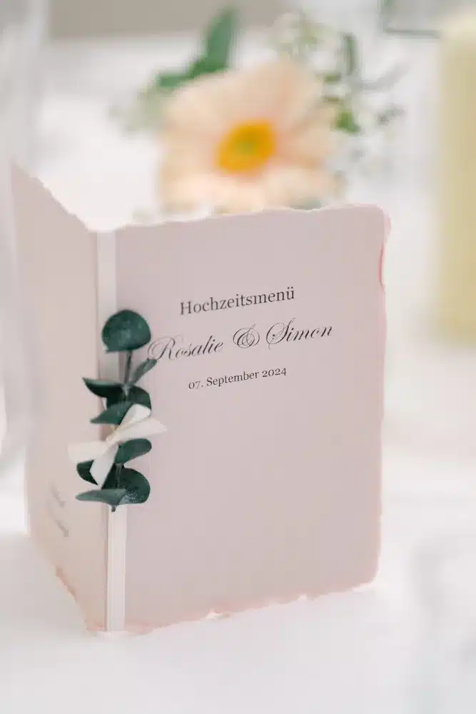 Rosa Hochzeitsmenü-Karte mit Büttenrand, Eukalyptuszweig und Blüte auf der Hochzeitstafel in der Orangerie Eisenstadt