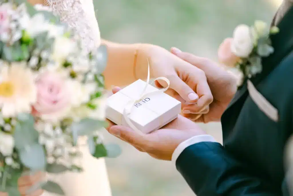 Bräutigam überreicht der Braut ein kleines weißes Geschenk mit Schleife, daneben der Brautstrauß, Hochzeit im Schlosspark Eisenstadt