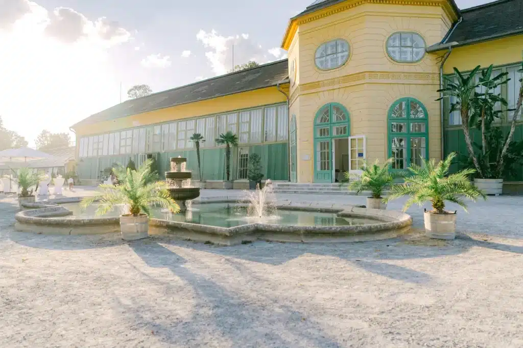 Gelbe Orangerie im Schlosspark Eisenstadt mit Springbrunnen und Palmen im warmen Abendlicht, Hochzeitslocation im Burgenland
