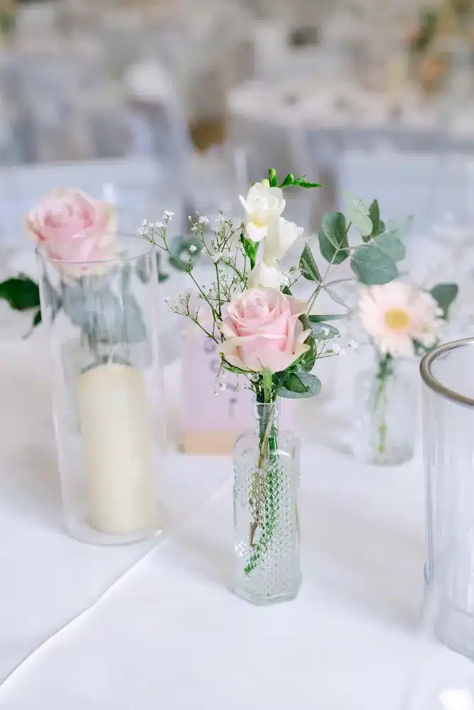 Rosafarbene Rosen und Dahlien in kleinen Glasvasen neben Kerzen auf der Hochzeitstafel in der Orangerie im Schlosspark Eisenstadt