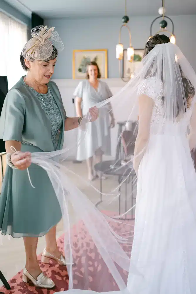 Begleiterin im grünen Kleid richtet den langen Schleier der Braut im Hotelzimmer, Getting Ready zur Hochzeit im Schlosspark Eisenstadt