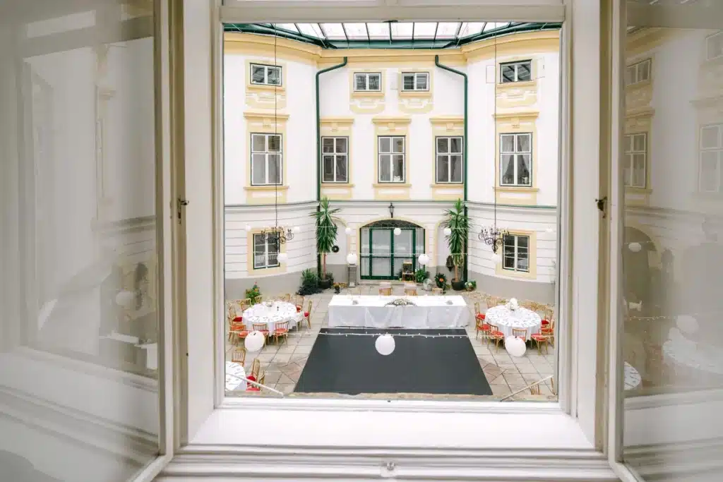 Heiraten in der Hochzeitslocation Schloss Margarethen am Moos – Details und Vorbereitungen: Blick durch ein Fenster auf den festlich dekorierten Schlosshof