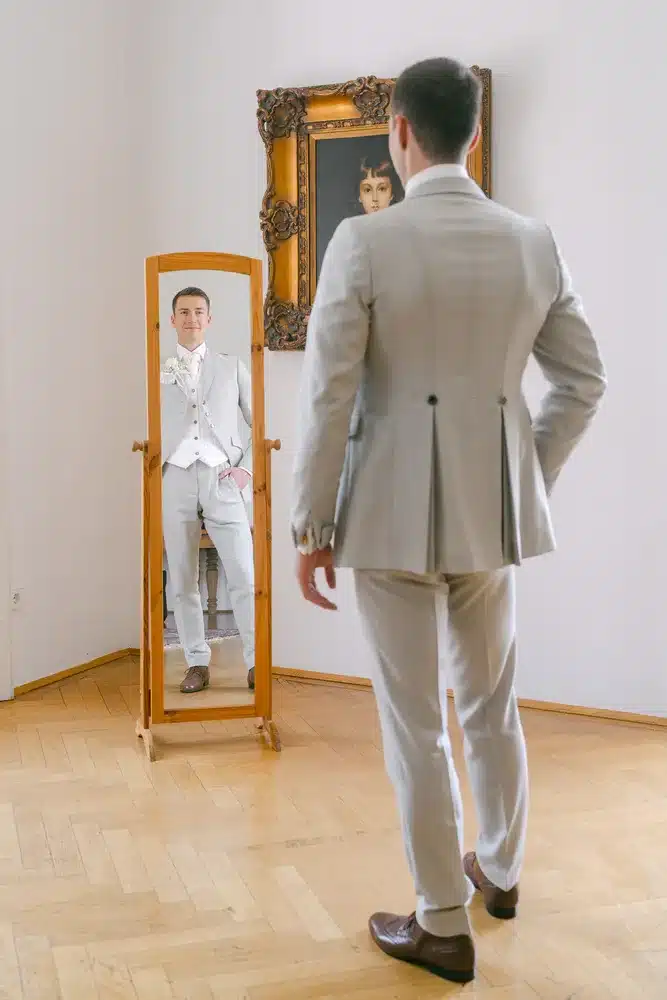 Heiraten in der Hochzeitslocation Schloss Margarethen am Moos – Getting Ready: Bräutigam steht vor einem Standspiegel mit Gemälde