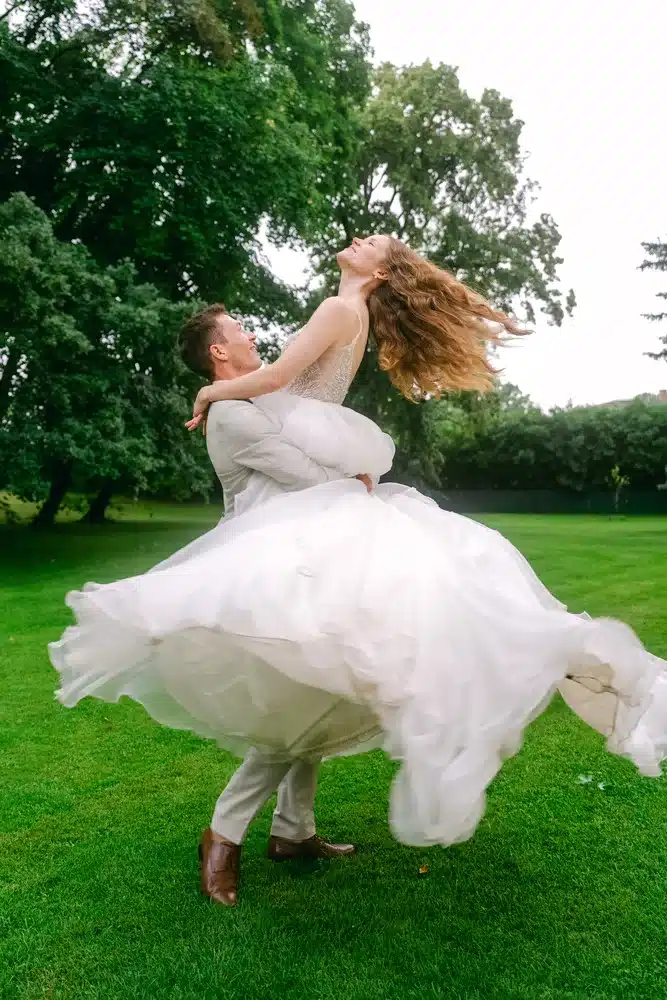 Heiraten in der Hochzeitslocation Schloss Margarethen am Moos – Brautpaarshooting: Bräutigam wirbelt die Braut im Kreis auf der Wiese