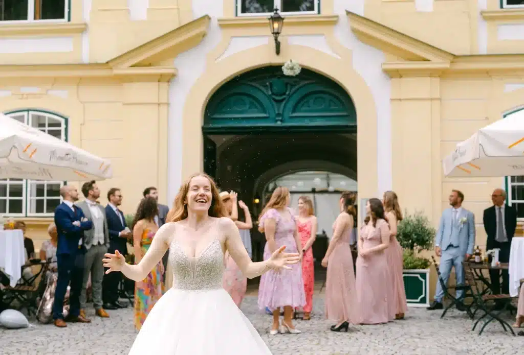 Heiraten in der Hochzeitslocation Schloss Margarethen am Moos – Gratulationen: Braut lacht mit ausgebreiteten Armen im Konfettiregen
