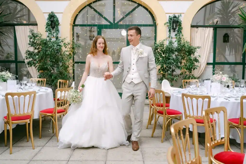 Heiraten in der Hochzeitslocation Schloss Margarethen am Moos – Gratulationen: Brautpaar geht Hand in Hand durch den Innenhof