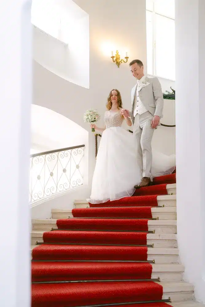 Heiraten in der Hochzeitslocation Schloss Margarethen am Moos – Gratulationen: Brautpaar geht die rote Teppichtreppe hinunter