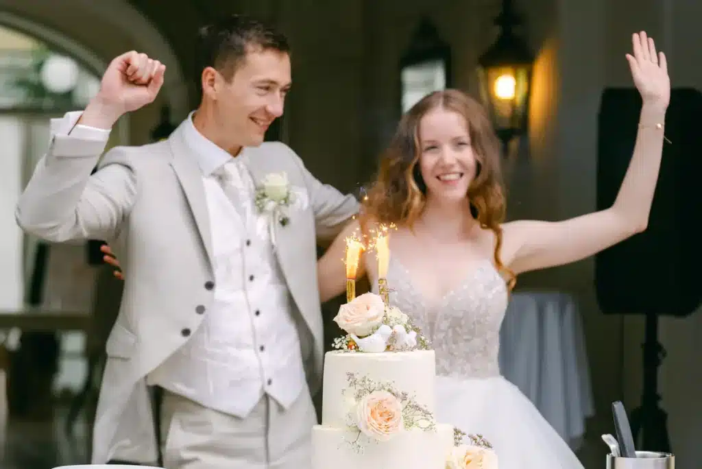 Heiraten in der Hochzeitslocation Schloss Margarethen am Moos – Feier, Hochzeitstanz und Party: Brautpaar jubelt hinter brennenden Wunderkerzen an der Torte
