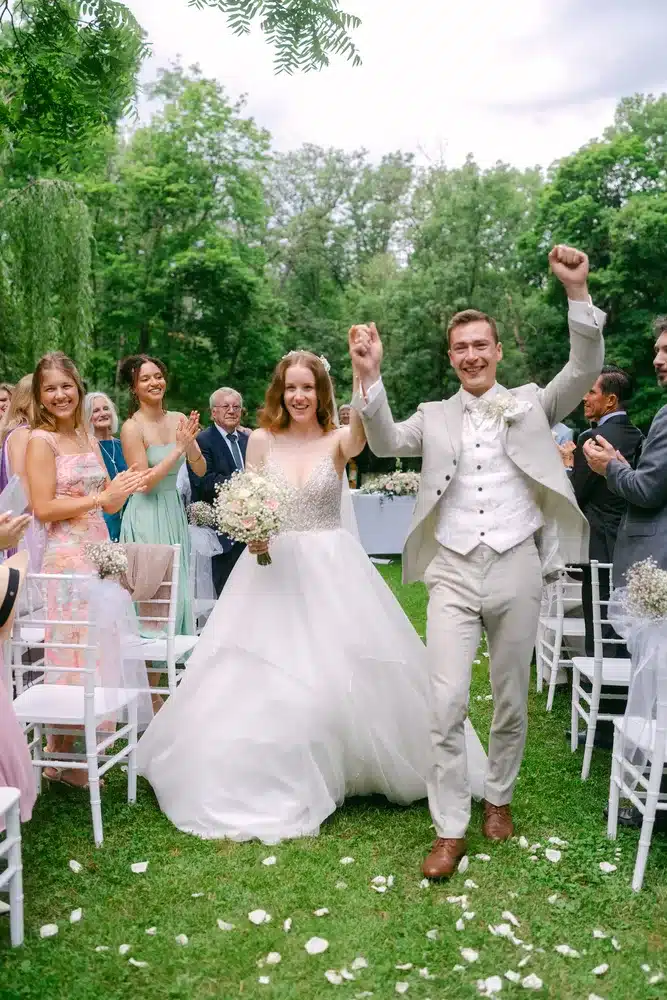 Heiraten in der Hochzeitslocation Schloss Margarethen am Moos – Brautpaarshooting: Brautpaar läuft jubelnd durch fallendes Laub