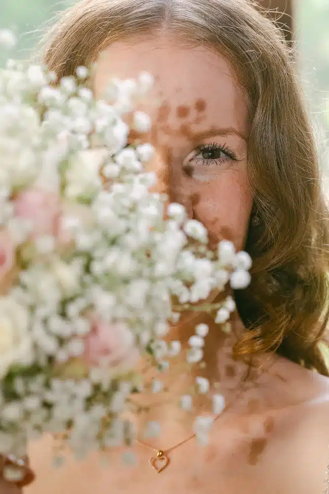 Heiraten in der Hochzeitslocation Schloss Margarethen am Moos – Getting Ready: Nahaufnahme des Brautgesichts hinter Schleierkraut und Strauß