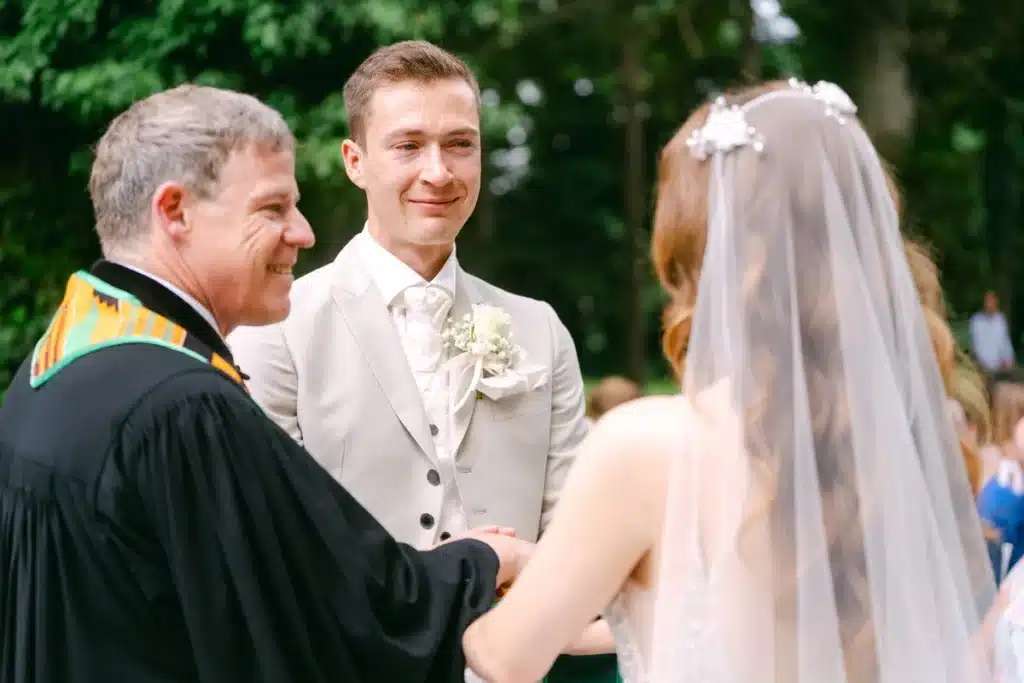 Heiraten in der Hochzeitslocation Schloss Margarethen am Moos – Trauung: Pfarrer traut das Brautpaar vor grünem Hintergrund