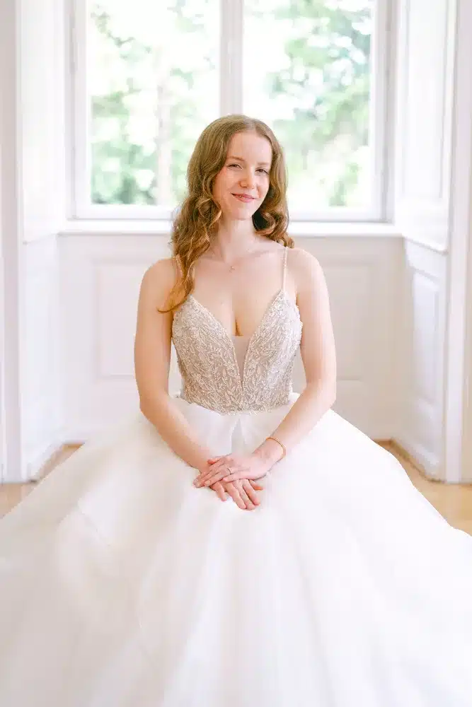 Heiraten in der Hochzeitslocation Schloss Margarethen am Moos – Getting Ready: Porträt der lächelnden Braut am Fenster