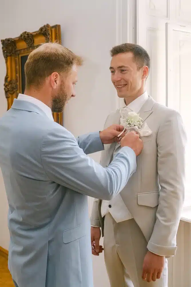 Heiraten in der Hochzeitslocation Schloss Margarethen am Moos – Getting Ready: Trauzeuge steckt dem Bräutigam die Ansteckblume an