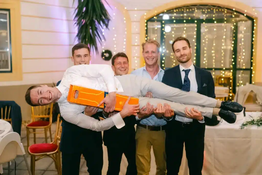 Heiraten in der Hochzeitslocation Schloss Margarethen am Moos – Gratulationen: Vier Männer tragen lachend einen Mann waagrecht