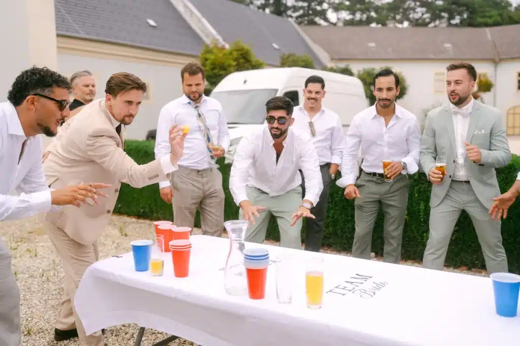 Männer in hellen Anzügen stehen jubelnd um den Bierpong-Tisch