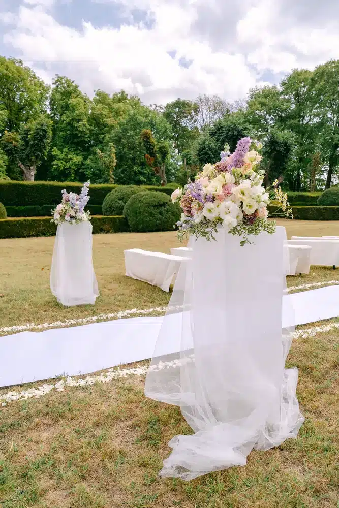 Blumengesteck in Pastelltönen auf weißem Sockel neben dem weißen Läufer im Schlossgarten