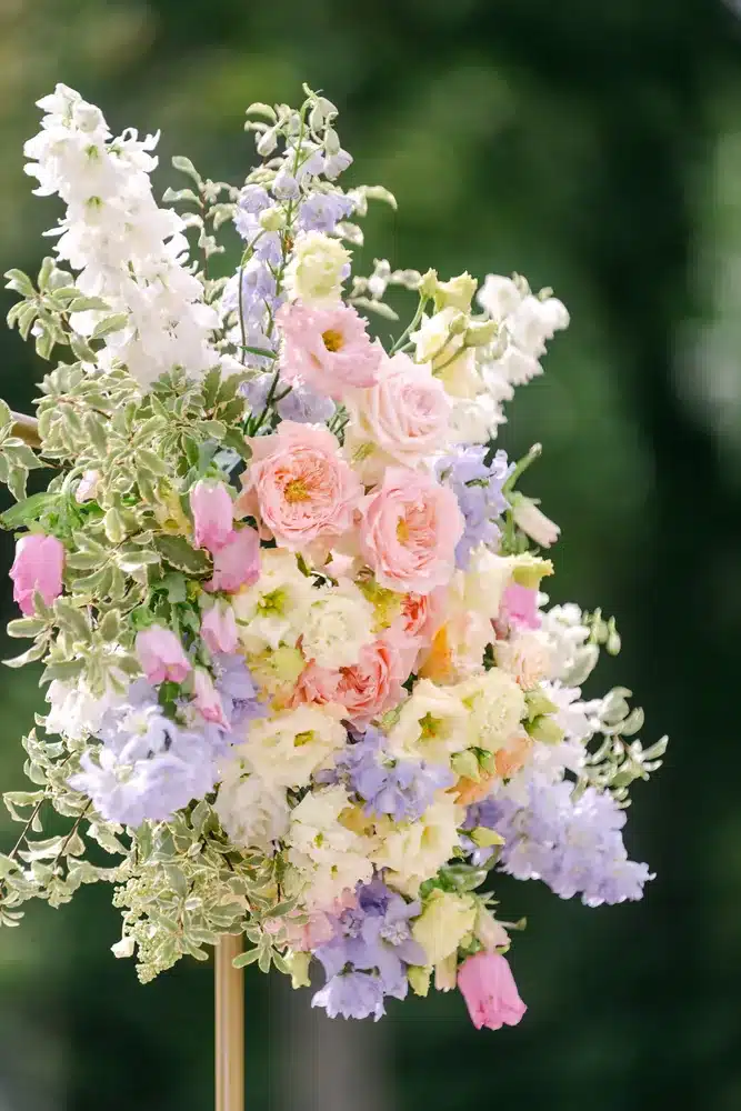 Blumengesteck aus Rosen und Blüten in Rosa, Flieder und Creme vor grünem Hintergrund
