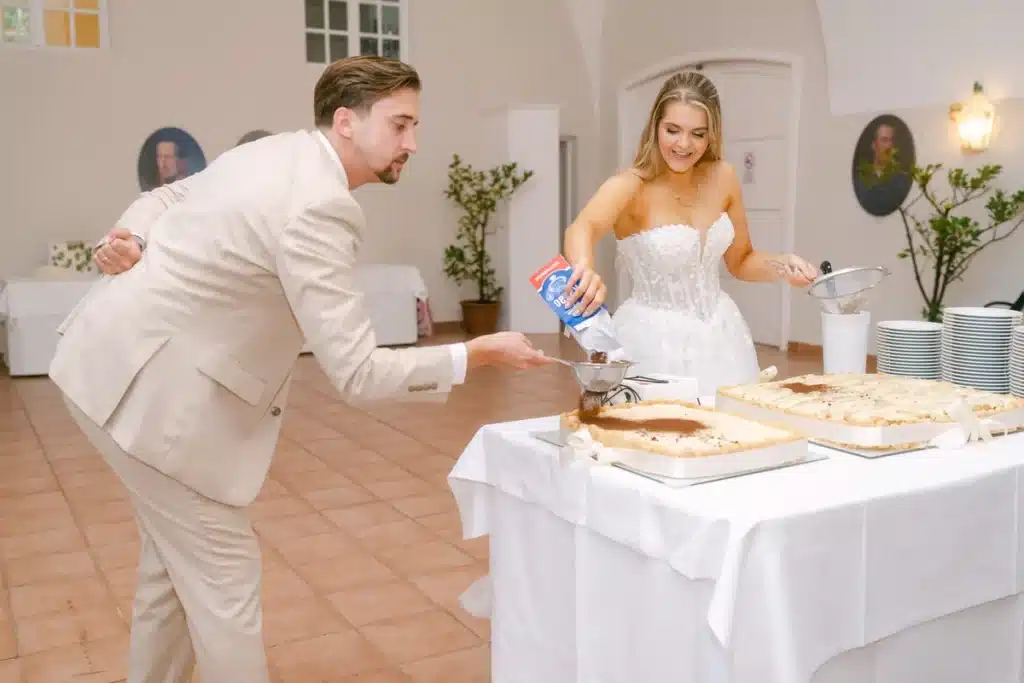 Bräutigam streut Pulver durch ein Sieb, das die Braut über das Tiramisu hält