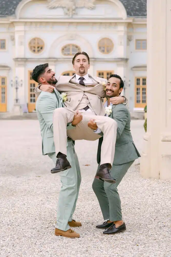 Zwei Freunde tragen den Bräutigam auf den Armen vor der Schlossfassade