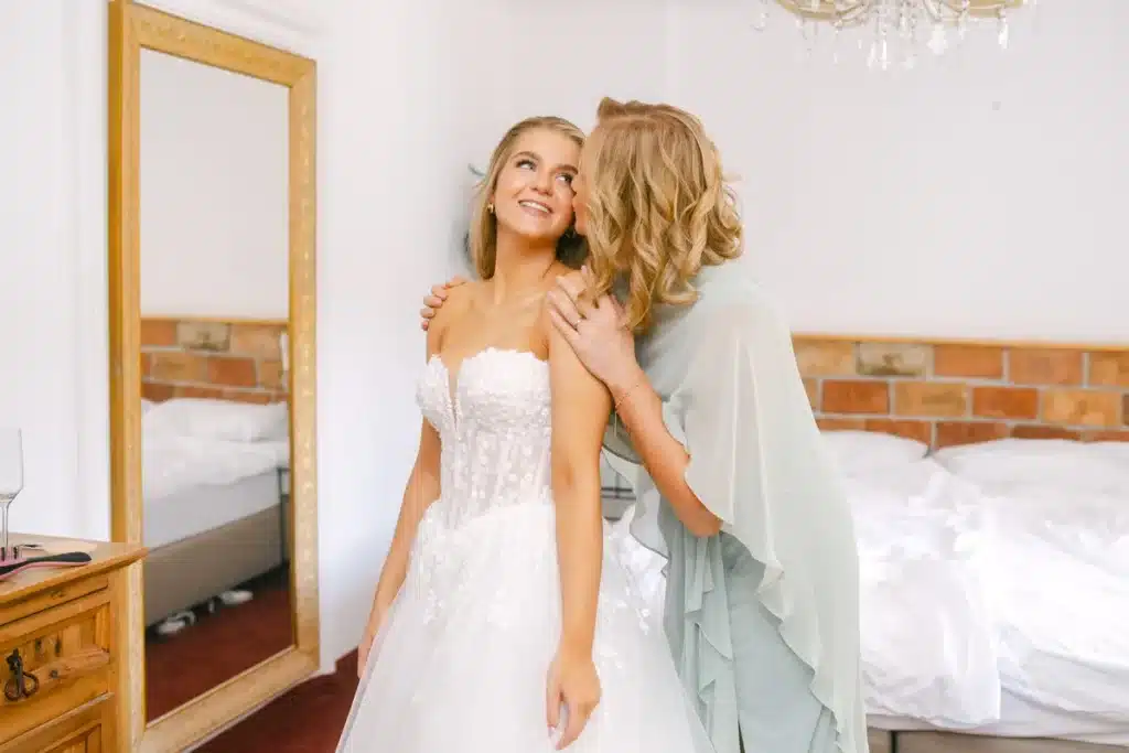 Braut im Brautkleid bekommt von einer Begleiterin im mintgrünen Kleid einen Kuss auf die Wange