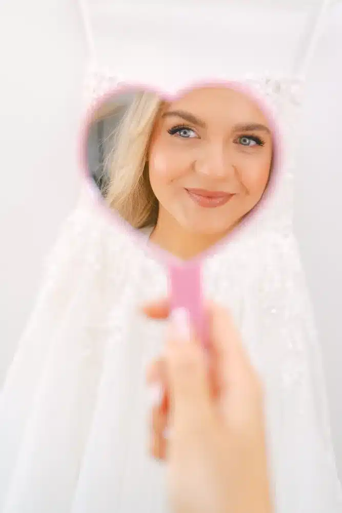 Spiegelbild der lächelnden Braut in einem rosa Handspiegel in Herzform