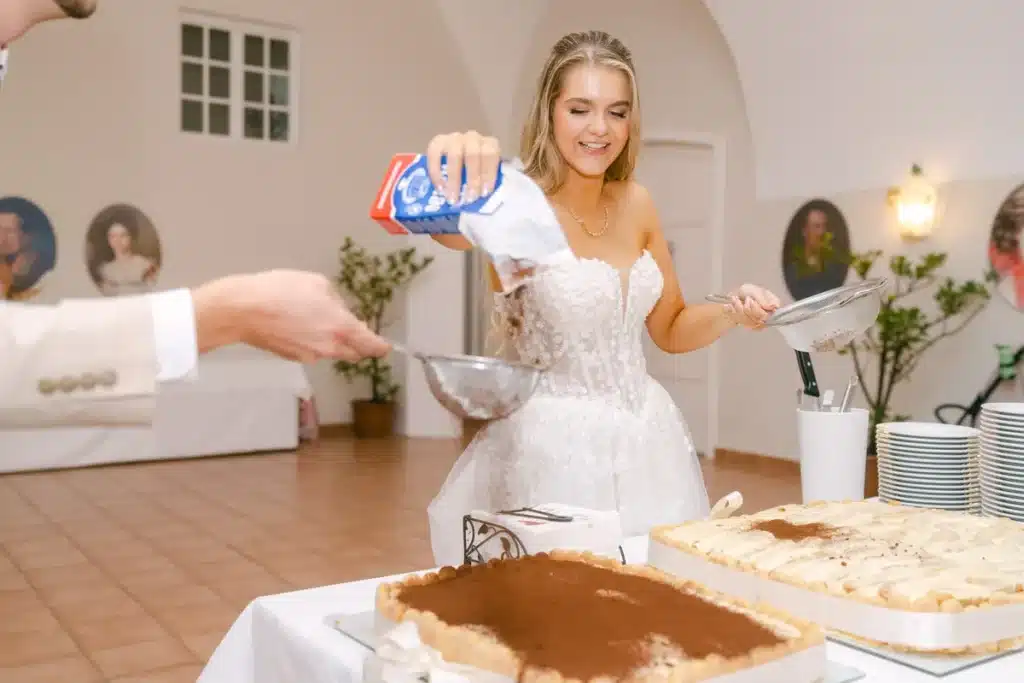 Braut streut lachend Pulver durch ein Sieb, davor das Tiramisu mit Kakao
