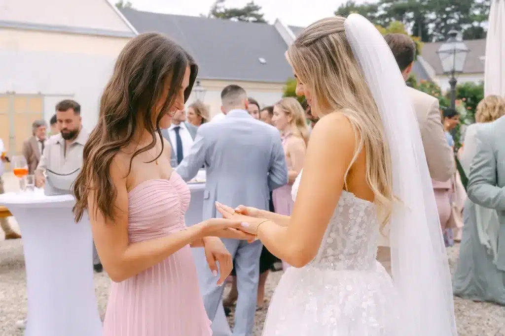 Brautjungfer im rosa Kleid betrachtet den Ehering an der Hand der Braut