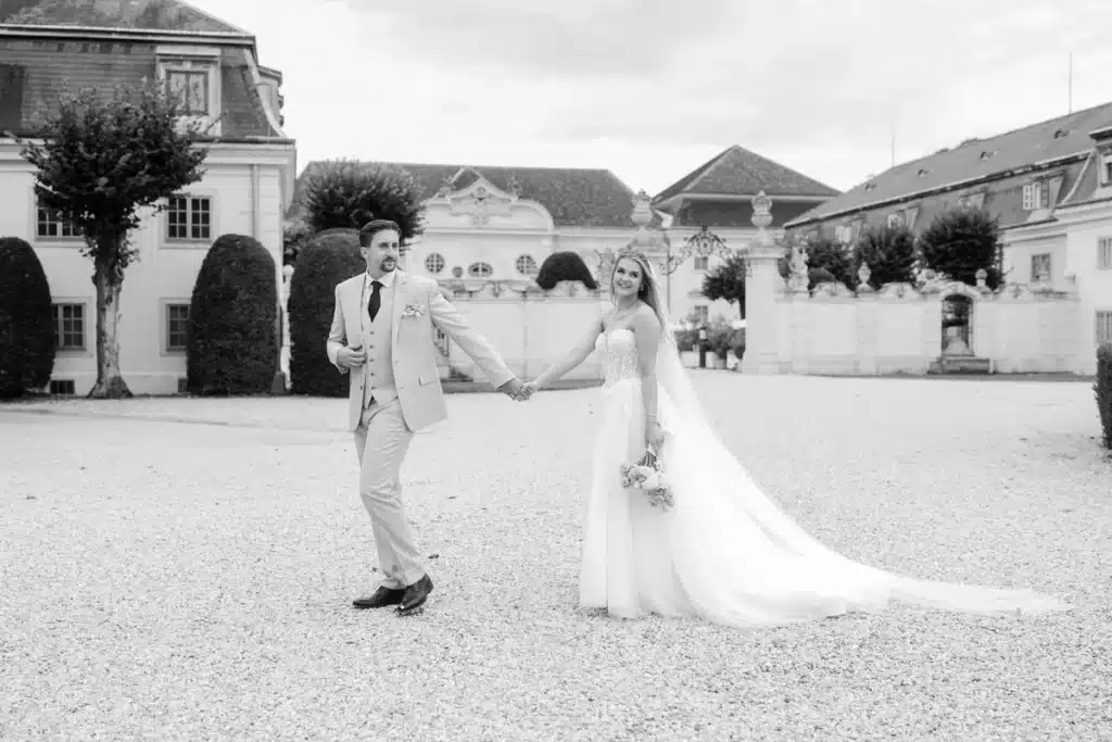Schwarzweißfoto des Brautpaares Hand in Hand im Schlosshof mit langer Schleppe