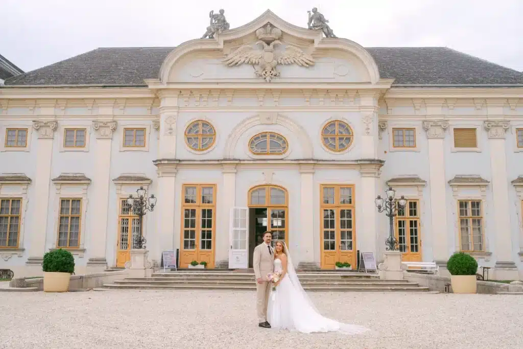 Brautpaar steht vor dem barocken Eingangsportal von Schloss Halbturn