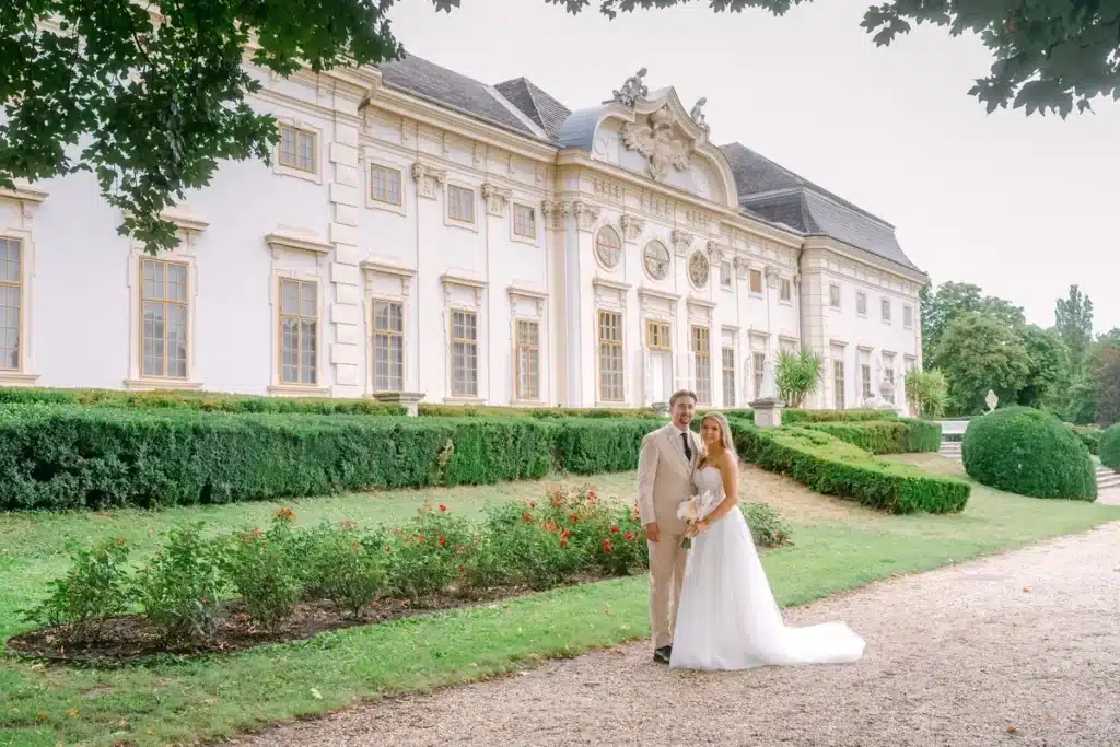 Brautpaar geht am Rosenbeet entlang vor der Fassade von Schloss Halbturn