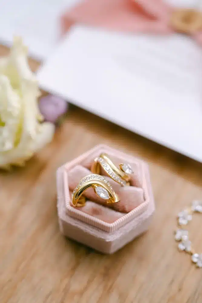 Zwei goldene Eheringe in einer rosa Samt-Ringbox auf einem Holztisch