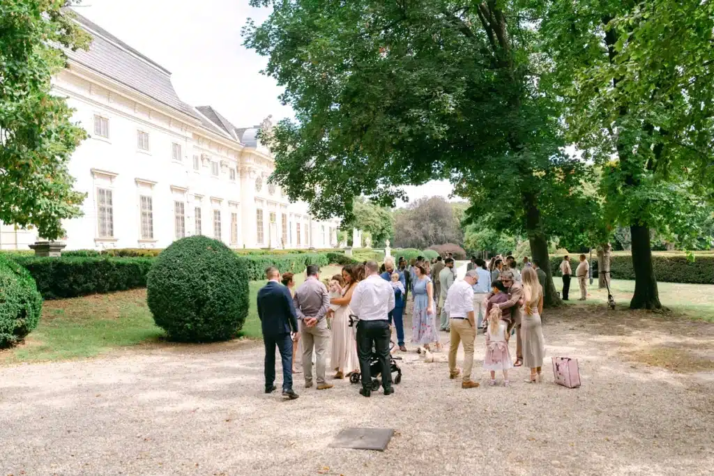 Hochzeitsgäste versammeln sich unter alten Bäumen vor Schloss Halbturn