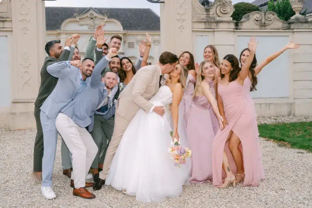 Gruppenfoto mit Brautjungfern und Freunden, das Brautpaar küsst sich in der Mitte