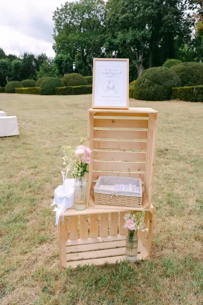 Gestapelte Holzkisten mit gerahmtem Schild, Blumen und Körbchen als Deko im Schlossgarten