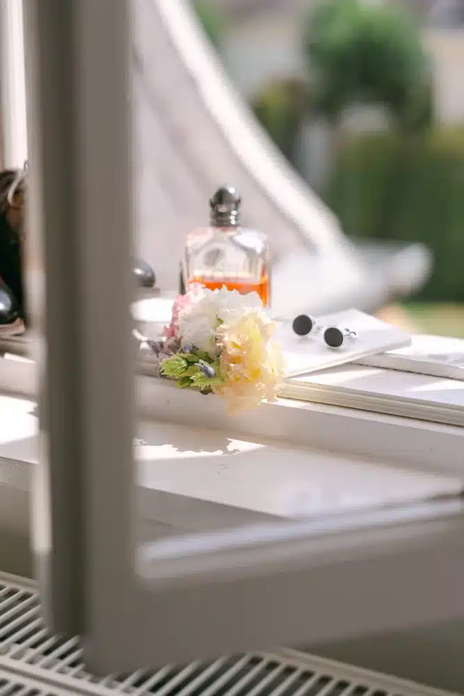 Parfumflasche und kleine Blüten auf der Fensterbank im Tageslicht