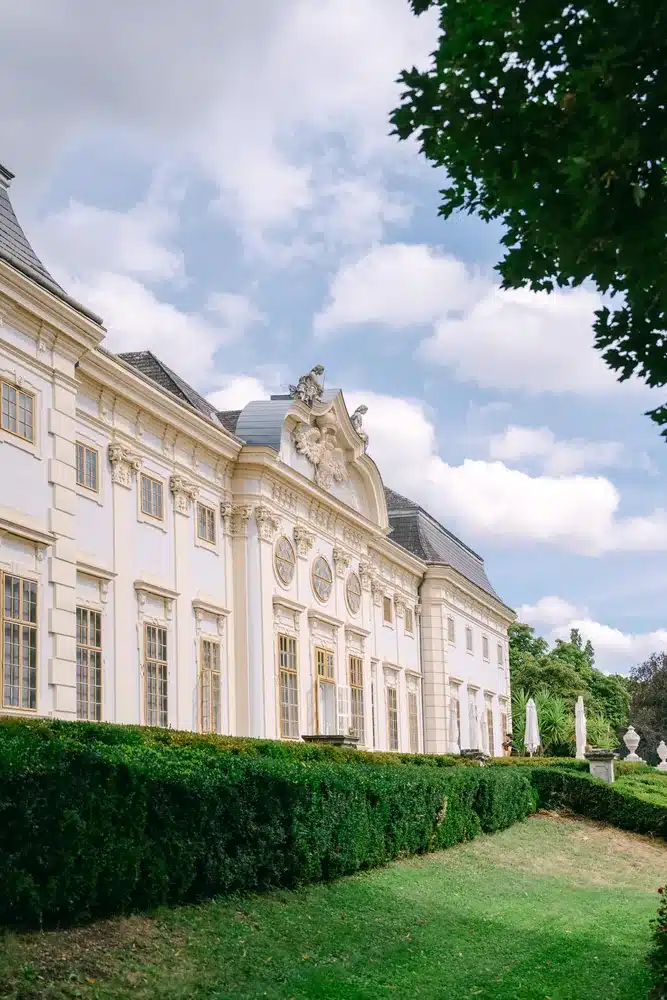 Barocke Fassade von Schloss Halbturn mit geschnittenen Buchsbaumhecken unter blauem Himmel