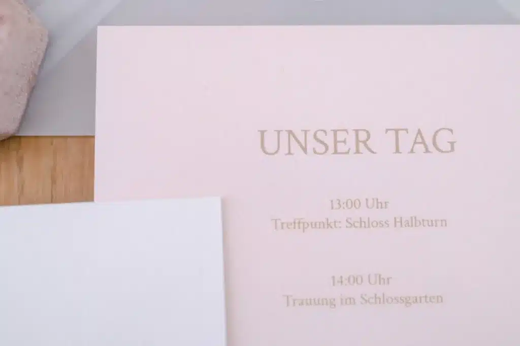 Tagesablauf-Karte in Rosa mit der Aufschrift Unser Tag, Treffpunkt Schloss Halbturn um 13 Uhr, Trauung im Schlossgarten um 14 Uhr